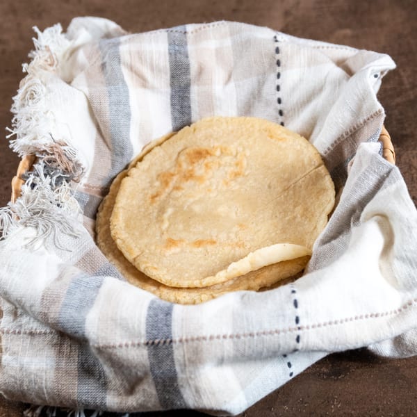 Warm corn tortillas in a woven basket lined with a striped cloth at Reyes Mexican Grill.