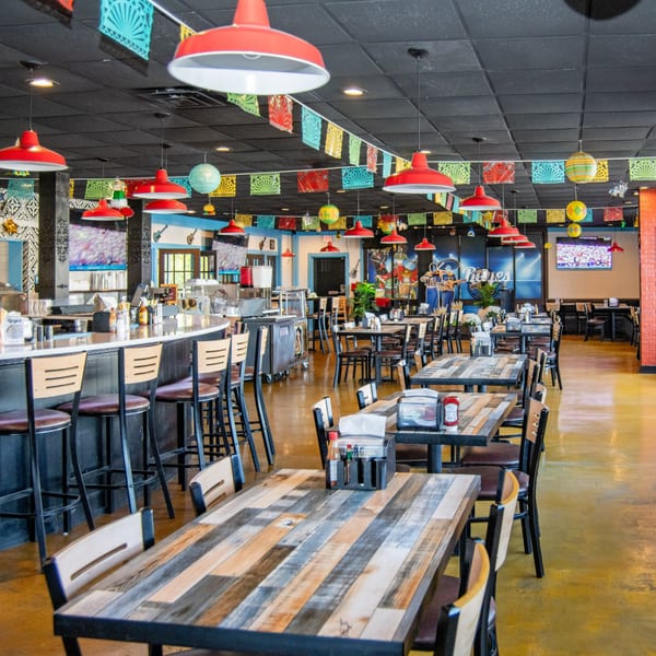 Spacious interior of Reyes Mexican Grill, featuring colorful papel picado, red pendant lights, and rustic wooden tables.