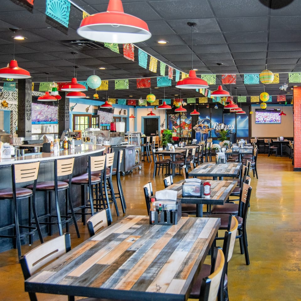 Spacious interior of Reyes Mexican Grill, featuring colorful papel picado, red pendant lights, and rustic wooden tables.