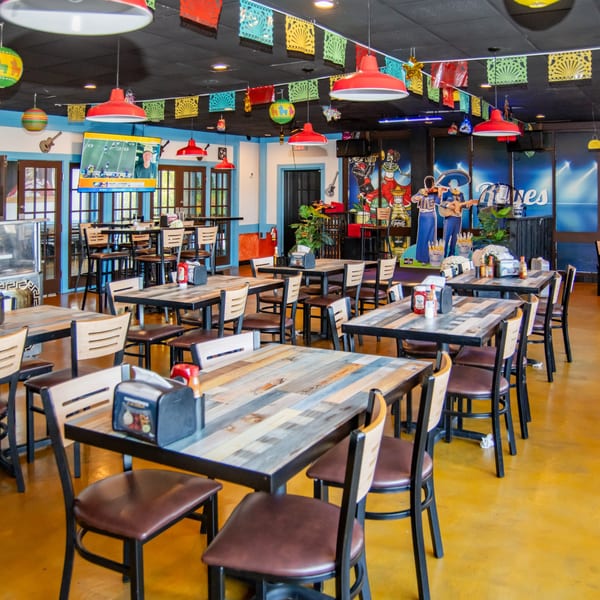 Vibrant interior of Reyes Mexican Grill with colorful papel picado, red lamps, and rustic wooden tables.