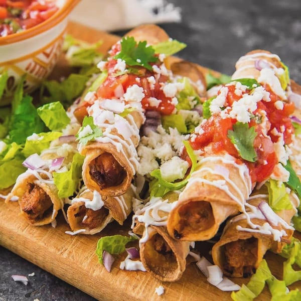 Crispy taquitos from Reyes Mexican Grill, topped with fresh lettuce, tomatoes, cheese, and a drizzle of crema.