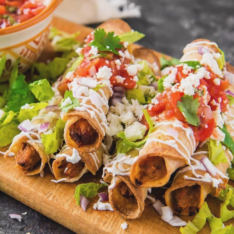Crispy taquitos from Reyes Mexican Grill, topped with fresh lettuce, tomatoes, cheese, and a drizzle of crema.